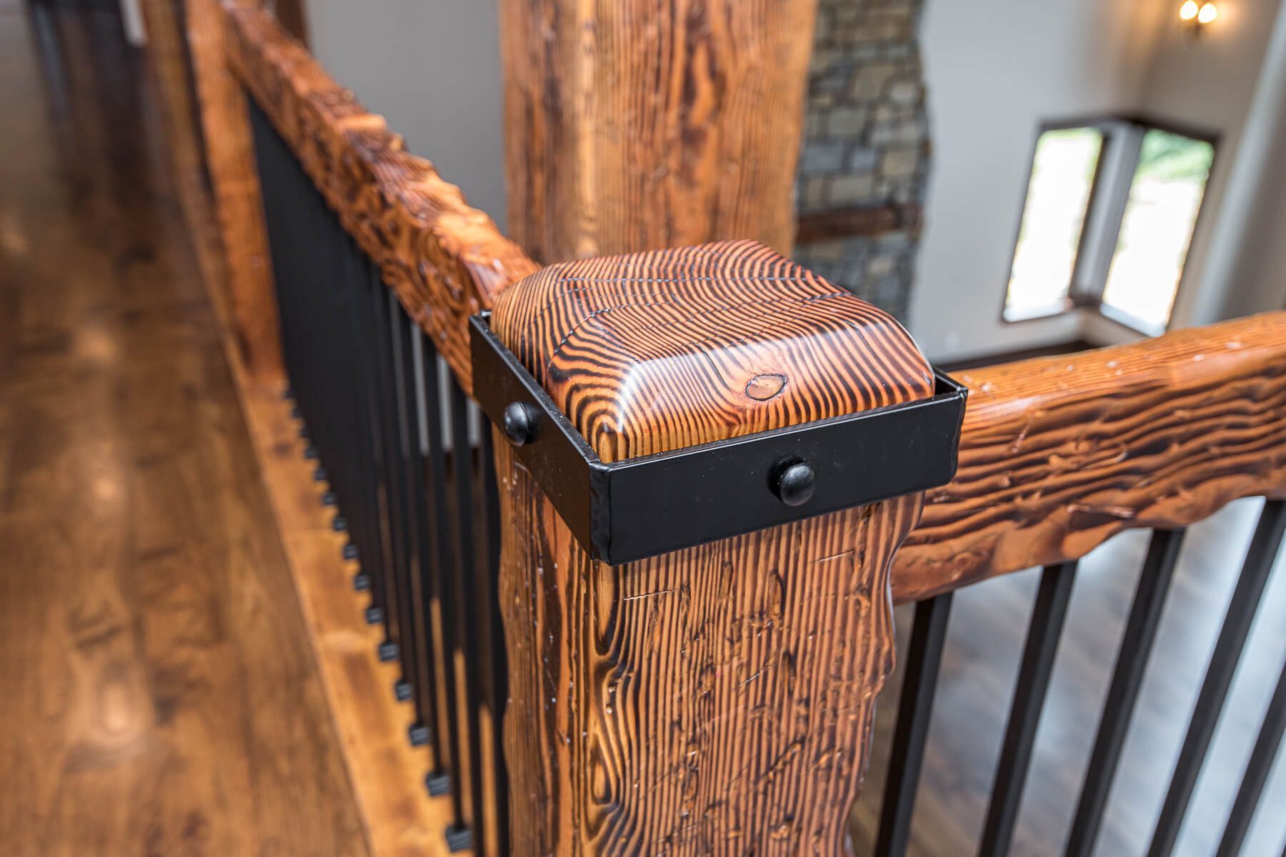 Close-up of a wooden stair railing with black metal spindles and corner post, interior setting.