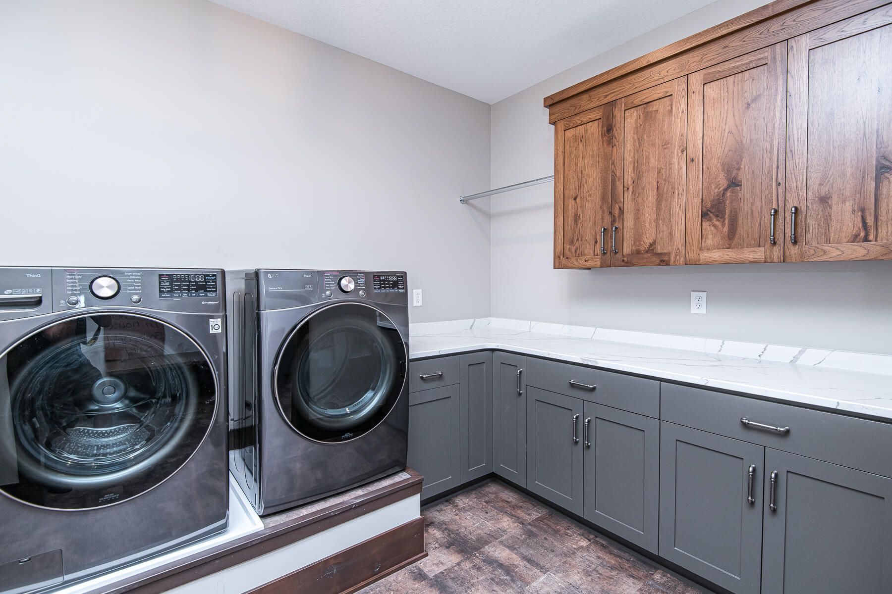 Laundry room with gray washer/dryer, cabinets, and wood-toned upper cabinets.