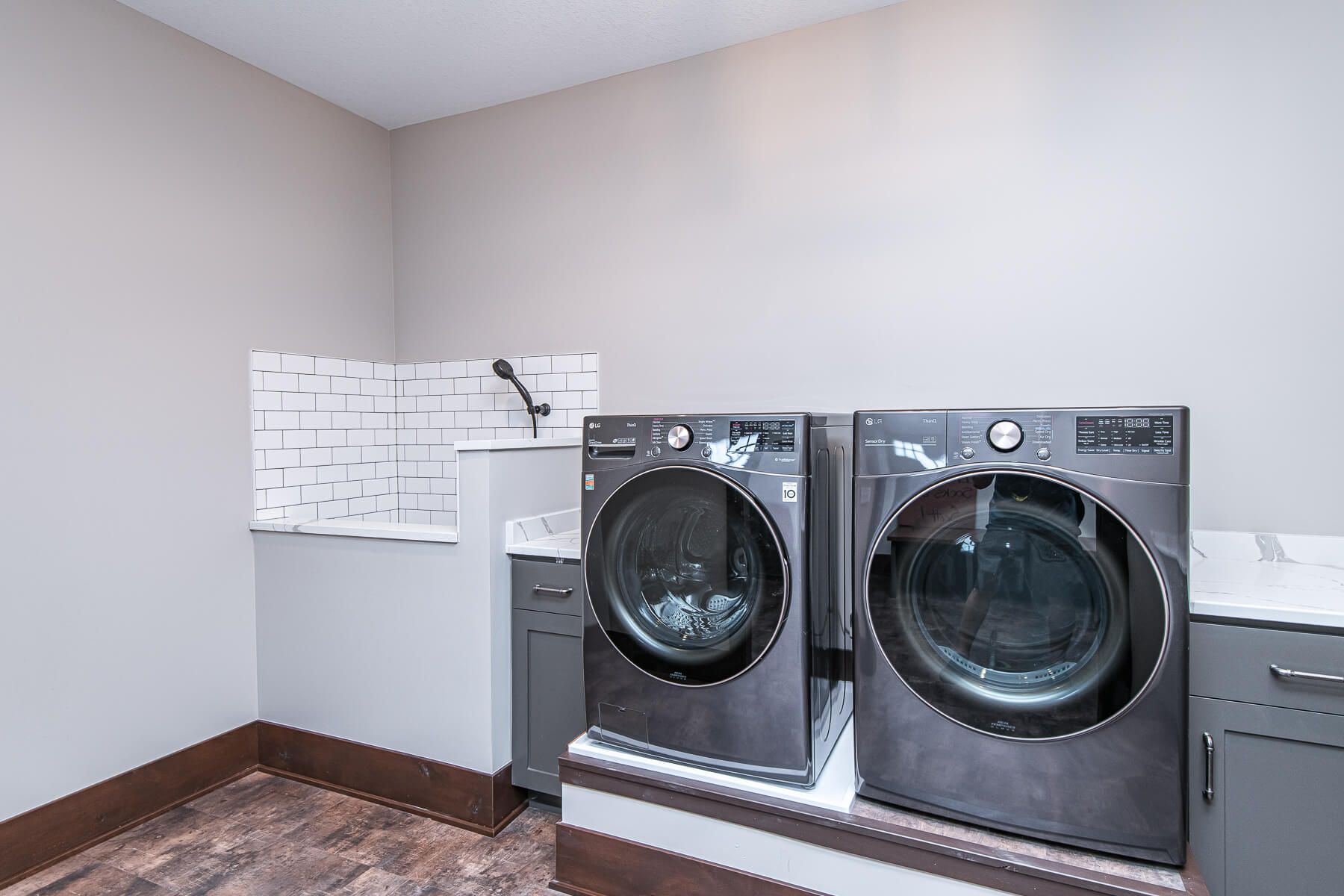 Laundry room with washer, dryer, dog wash station, and gray cabinets.