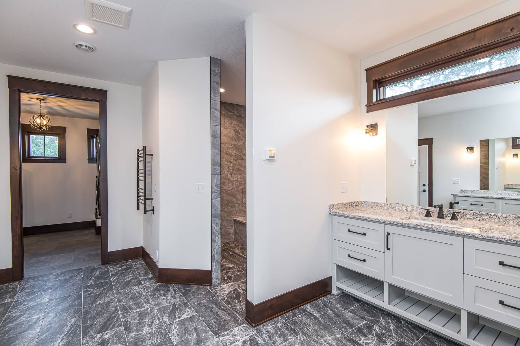 Spacious bathroom with white cabinets, granite countertop, and gray tiled floor; a walk-in shower.