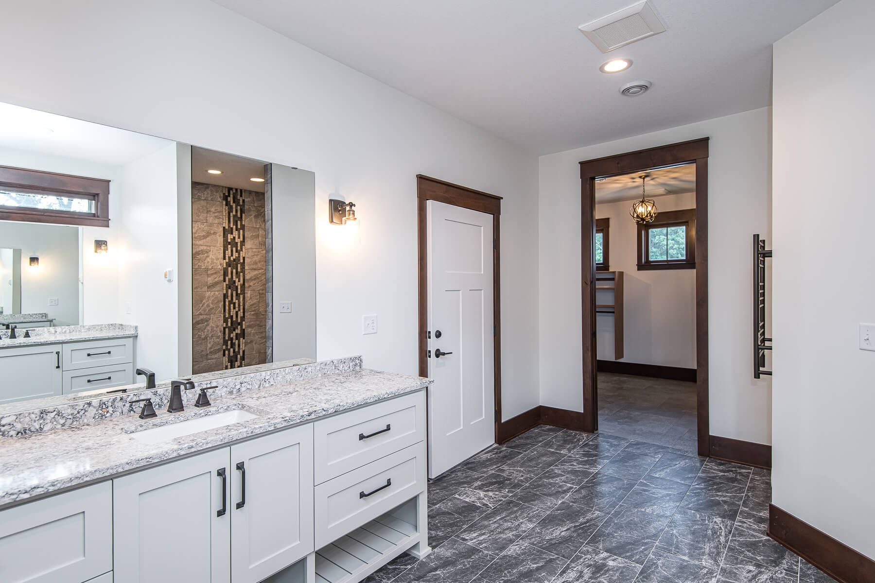 Bathroom with white cabinets, dark trim, and gray flooring. A doorway leads to another room.