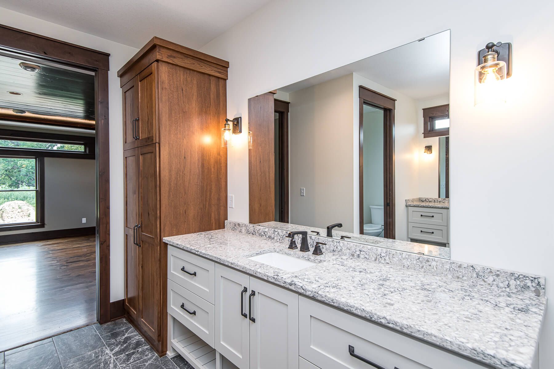 Bathroom with white vanity, granite countertop, tall wood cabinet, and large mirror.