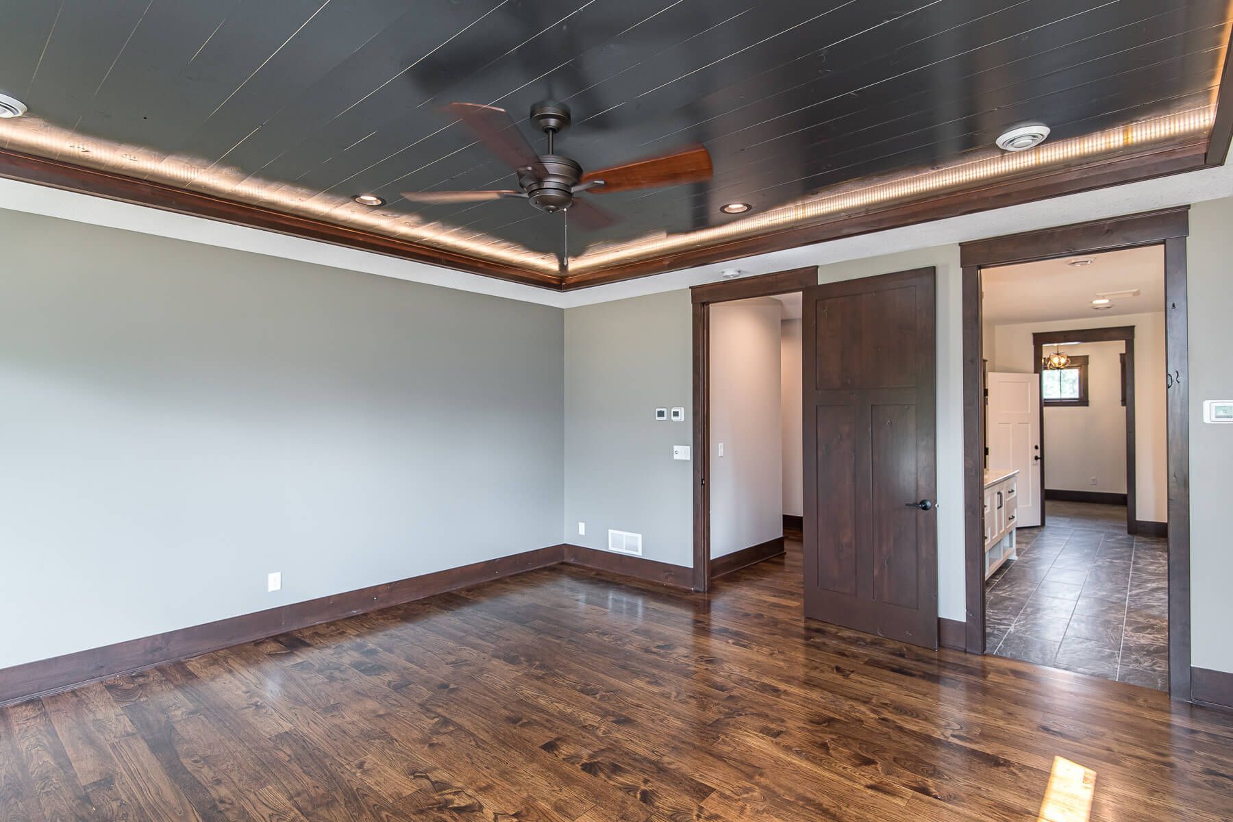 Empty room with dark wood trim, flooring, and ceiling with lighting; grey walls and doorways.