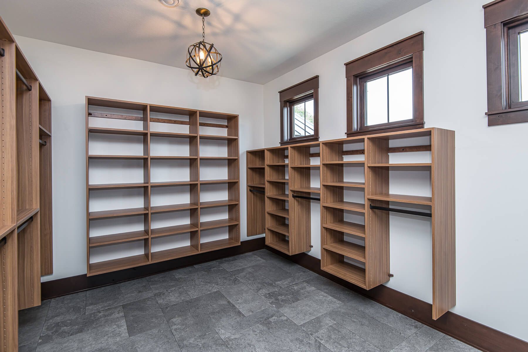 Empty walk-in closet with built-in wooden shelves on white walls, gray floor, two windows.