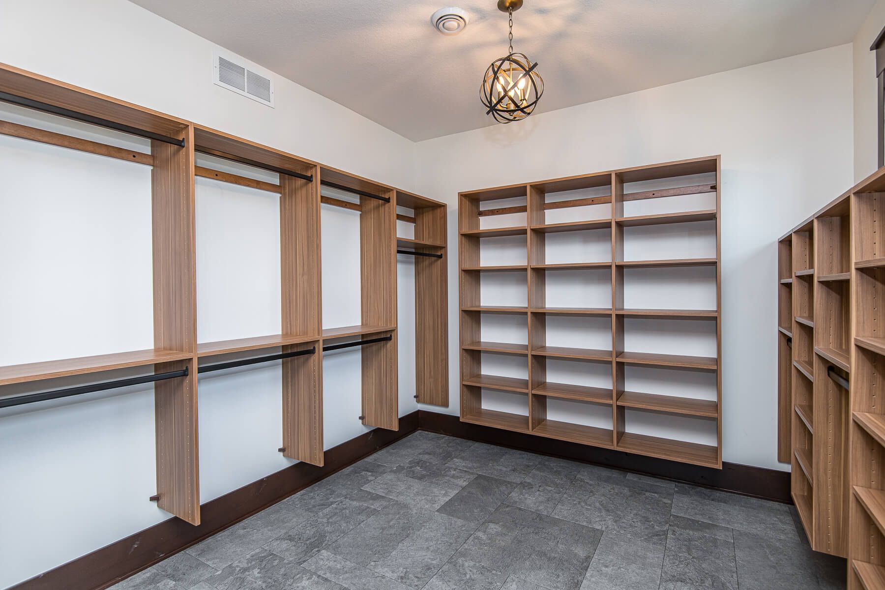 Empty walk-in closet with wooden shelving and hanging rods; gray carpet, white walls, and a decorative light fixture.