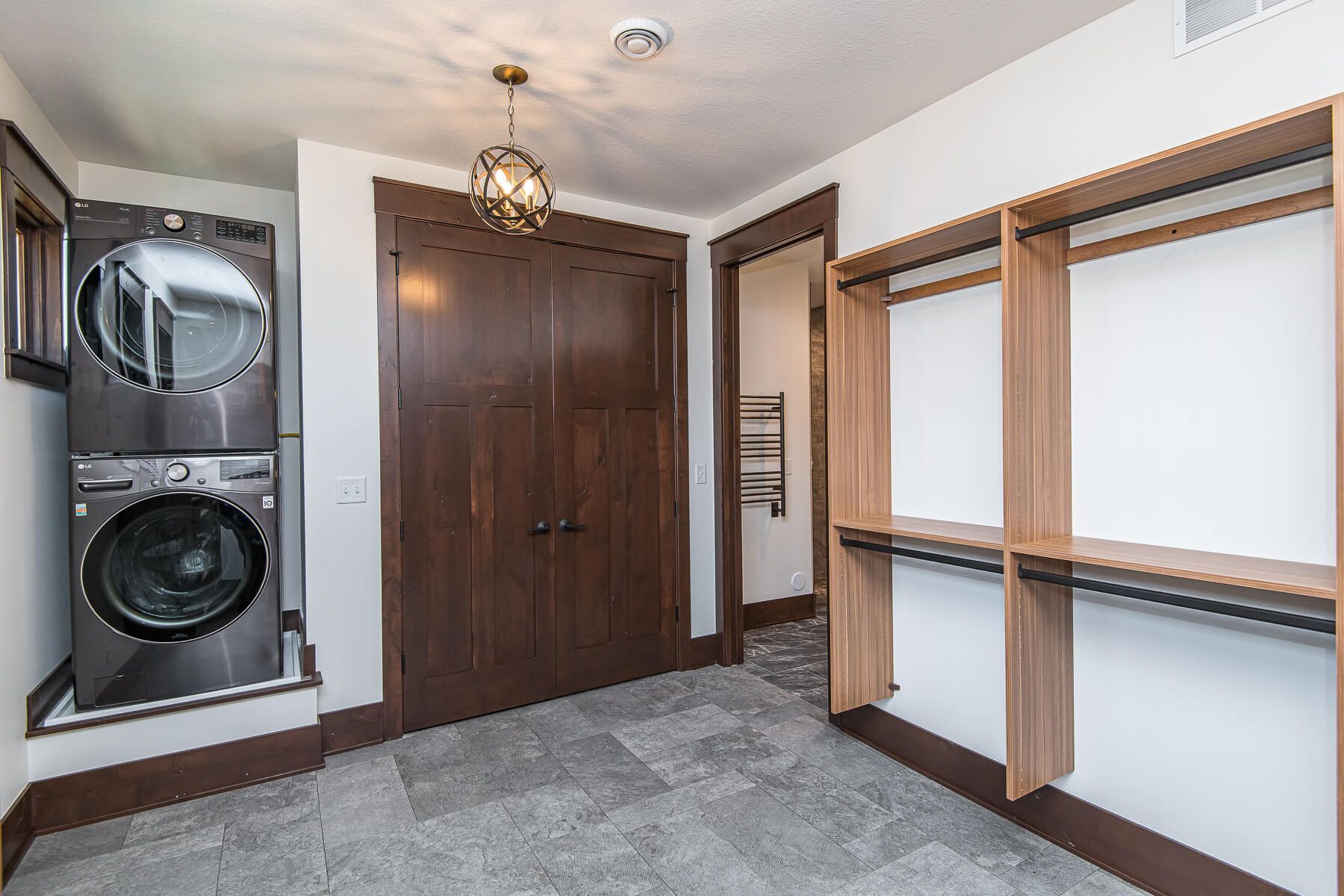 Laundry room with stacked washer/dryer, closet, and open shelving. Brown trim and a gray tiled floor.