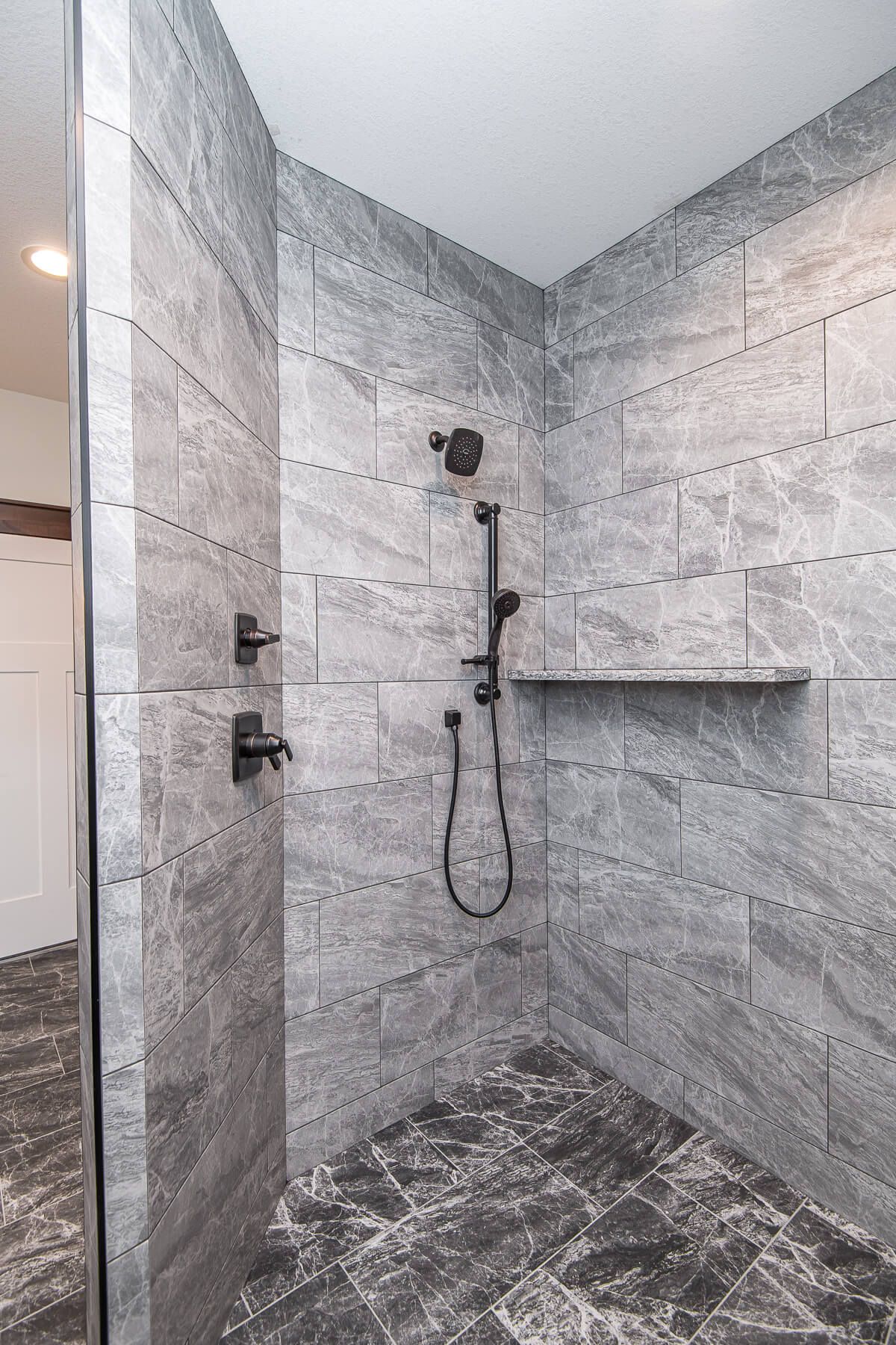 Gray-tiled shower with black fixtures and a built-in shelf.