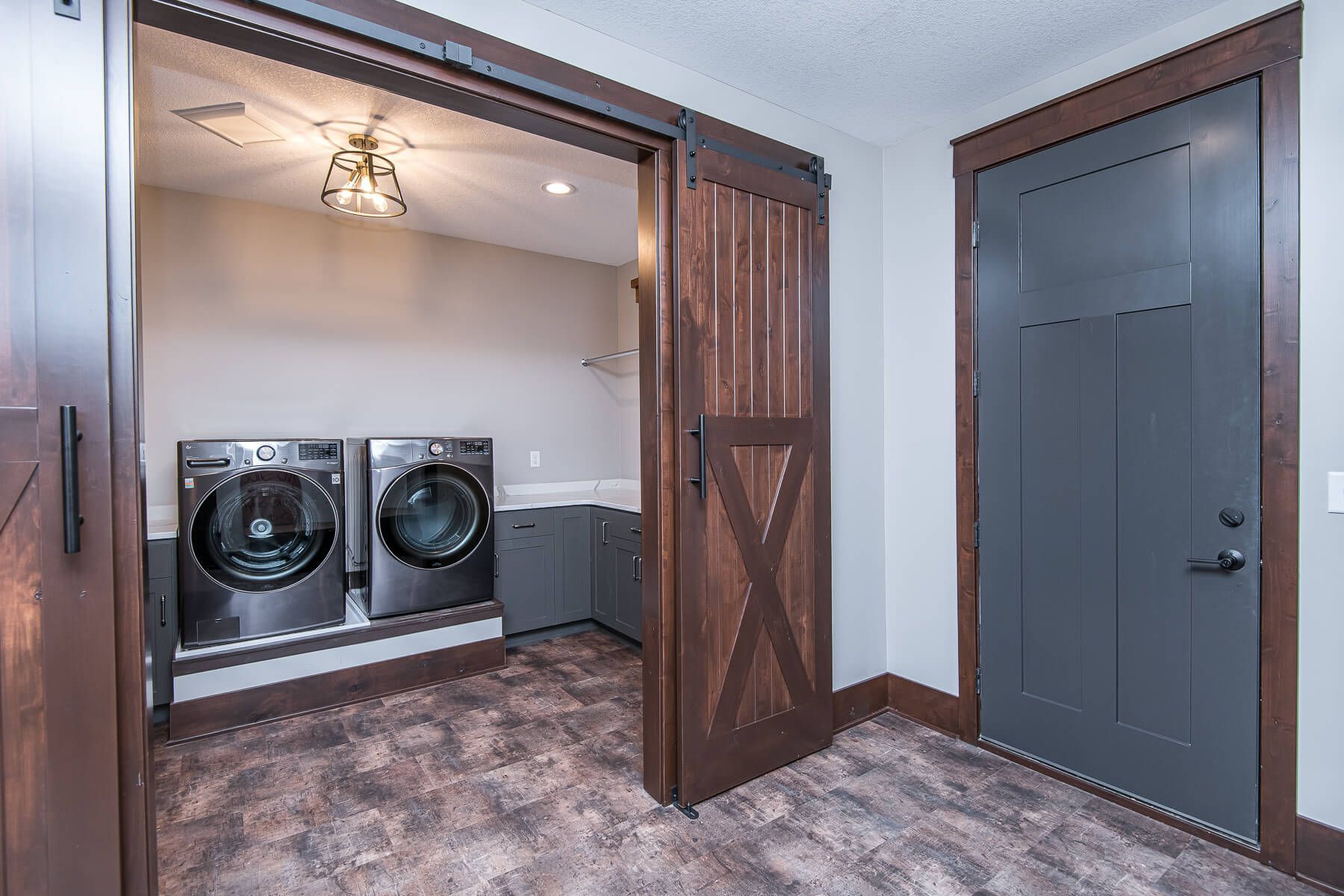 Laundry room with dark wood sliding door and gray door, showing washer/dryer, and a decorative light.