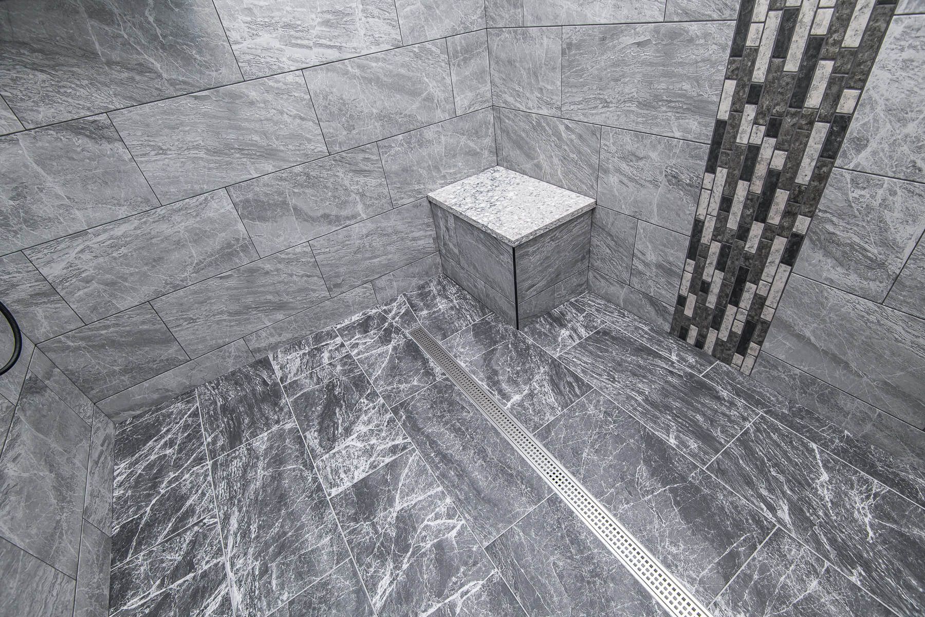 Gray tiled shower with a built-in seat and linear drain.