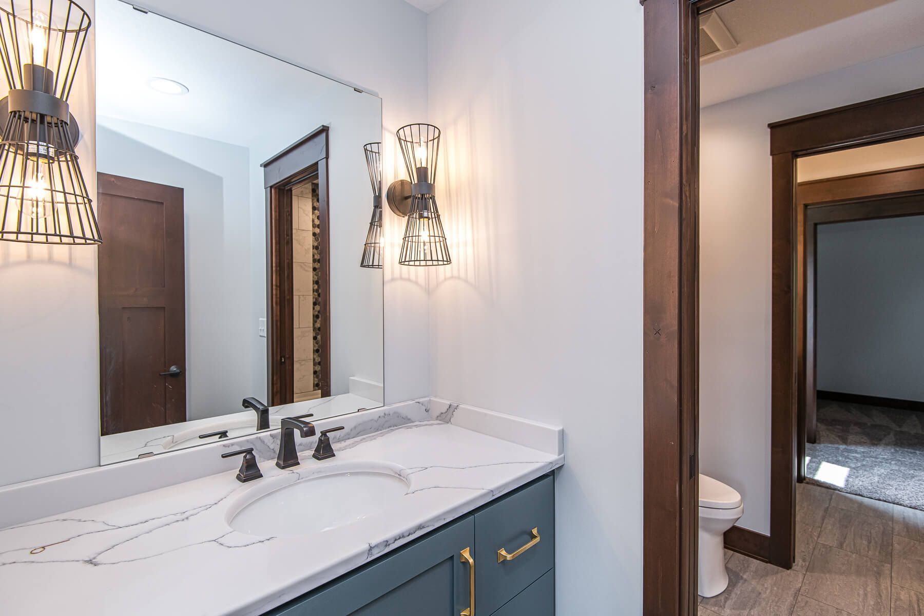 Bathroom vanity with a blue cabinet, marble countertop, large mirror, and two sconces.