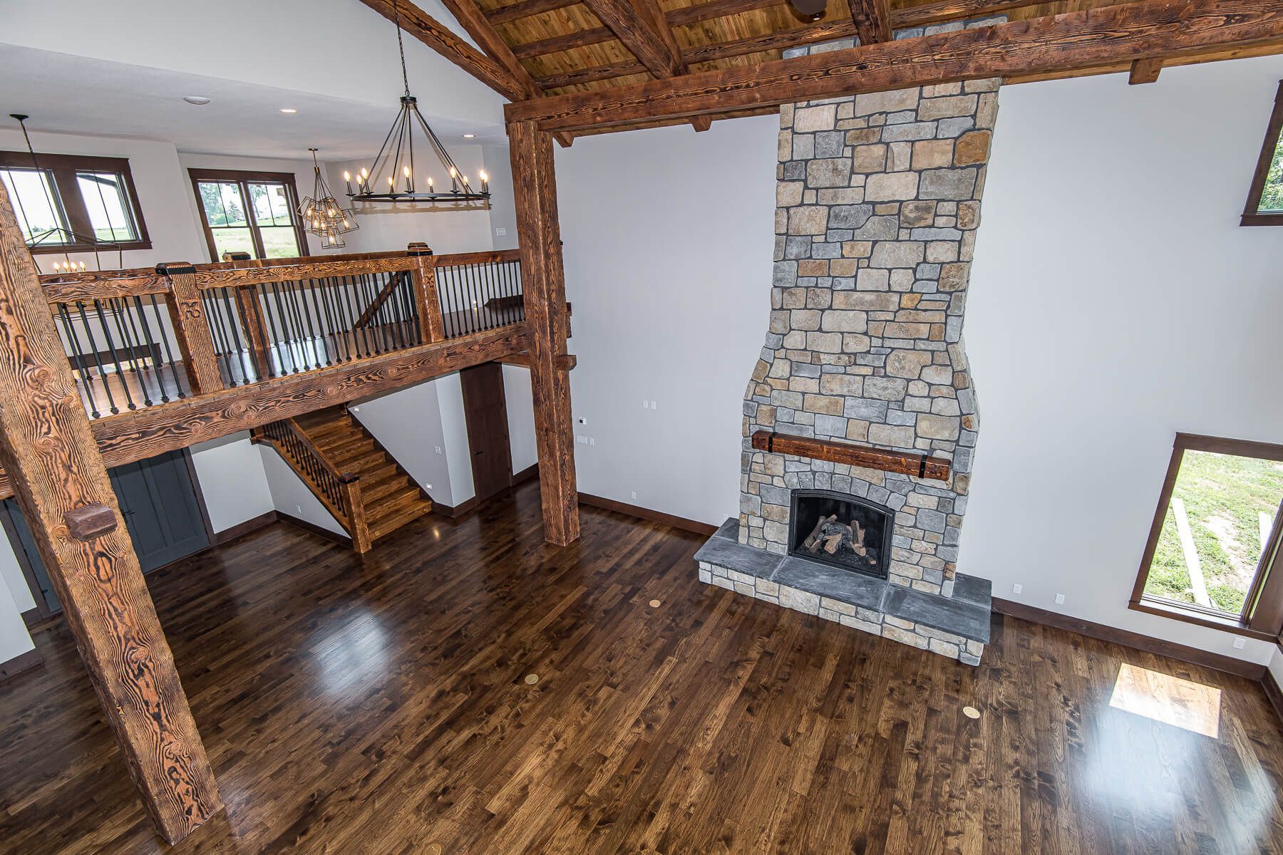 Spacious interior with stone fireplace, wooden beams, hardwood floors, and a loft.