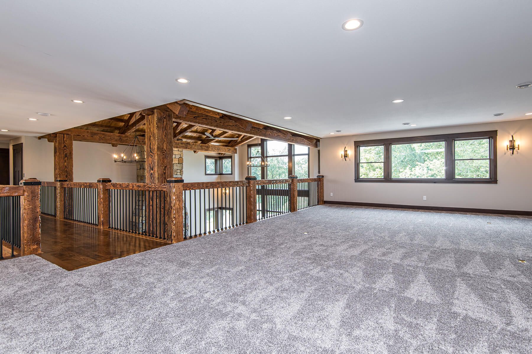 Loft area with light gray carpet, wooden railing, and decorative beam structure.