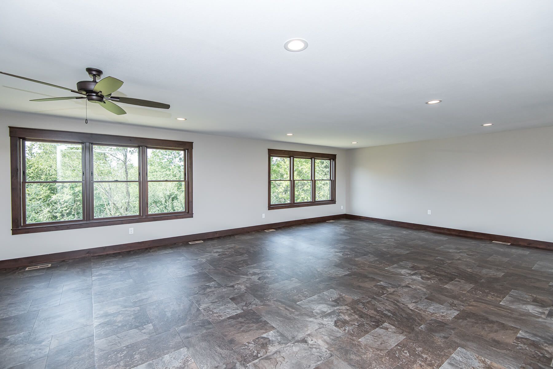 Empty room with dark wood trim, windows, and flooring. Ceiling fan and recessed lights.