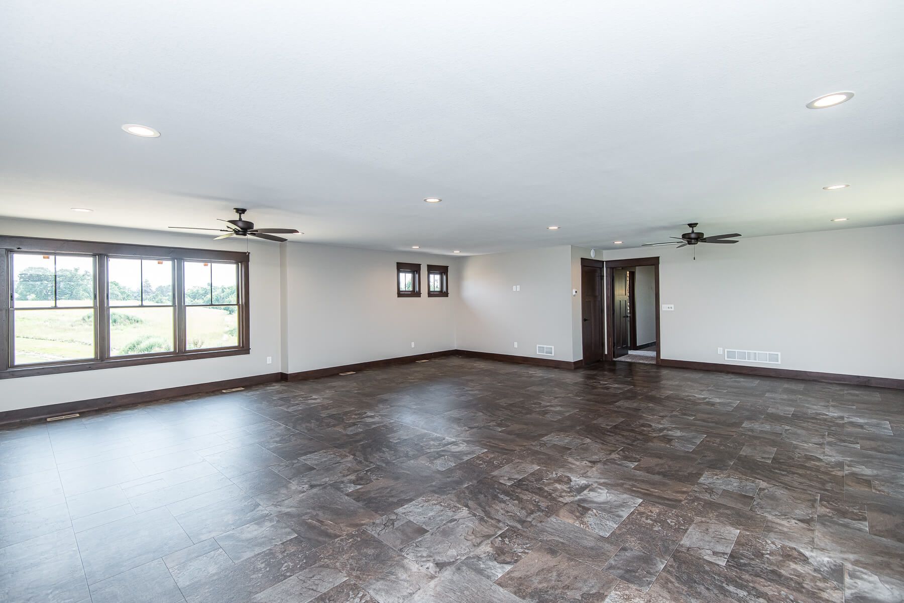 Empty, spacious room with dark flooring, multiple windows, recessed lighting, and ceiling fans.