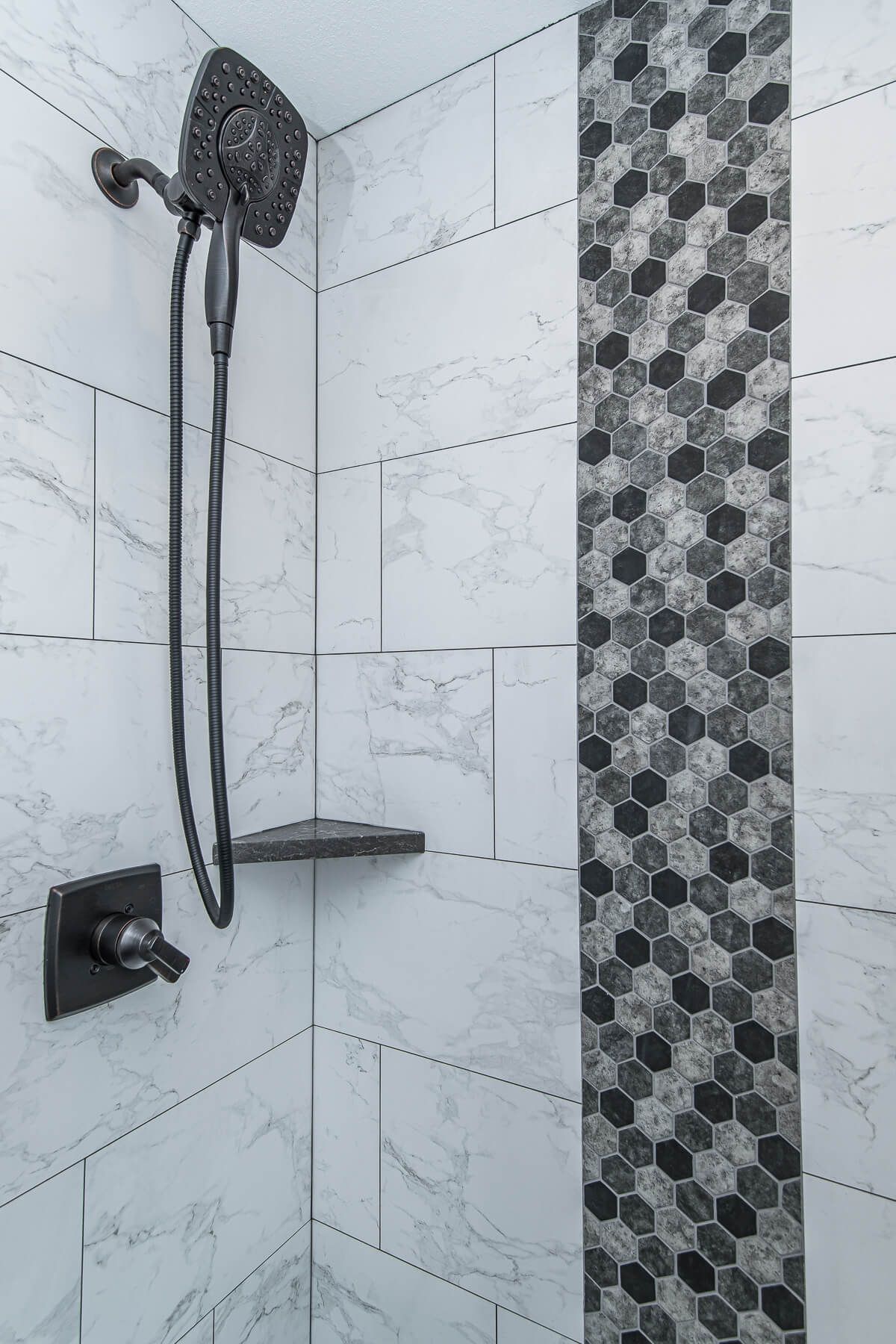 Shower with black fixtures and gray and white marble and patterned tile accents.
