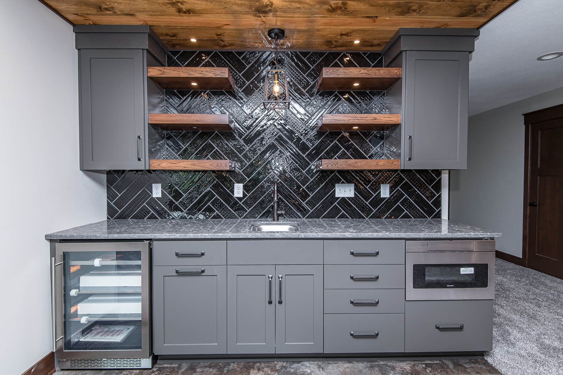 Gray home bar with cabinets, shelves, beverage cooler, microwave, and textured backsplash.