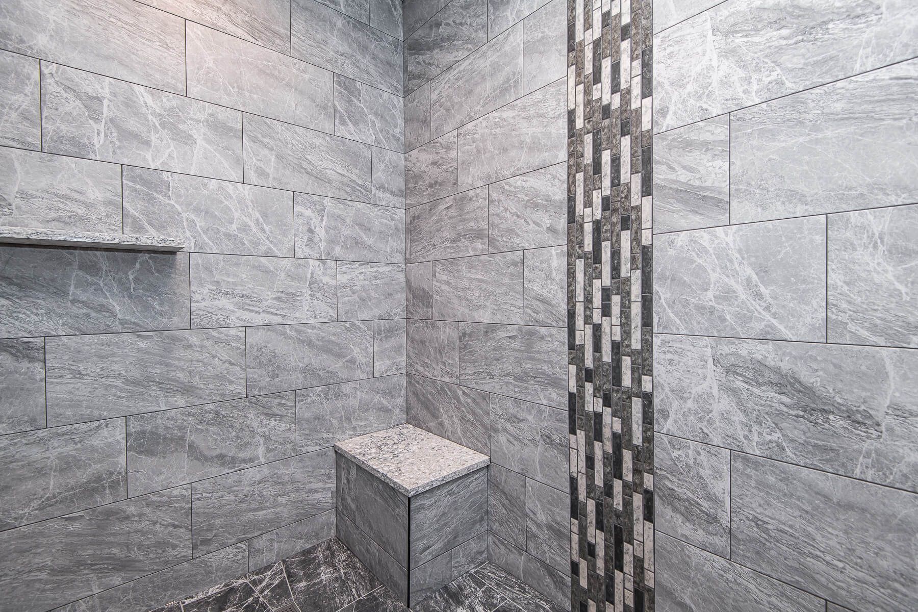 Gray tiled shower with built-in bench and shelf. Accent strip of black and white tiles.