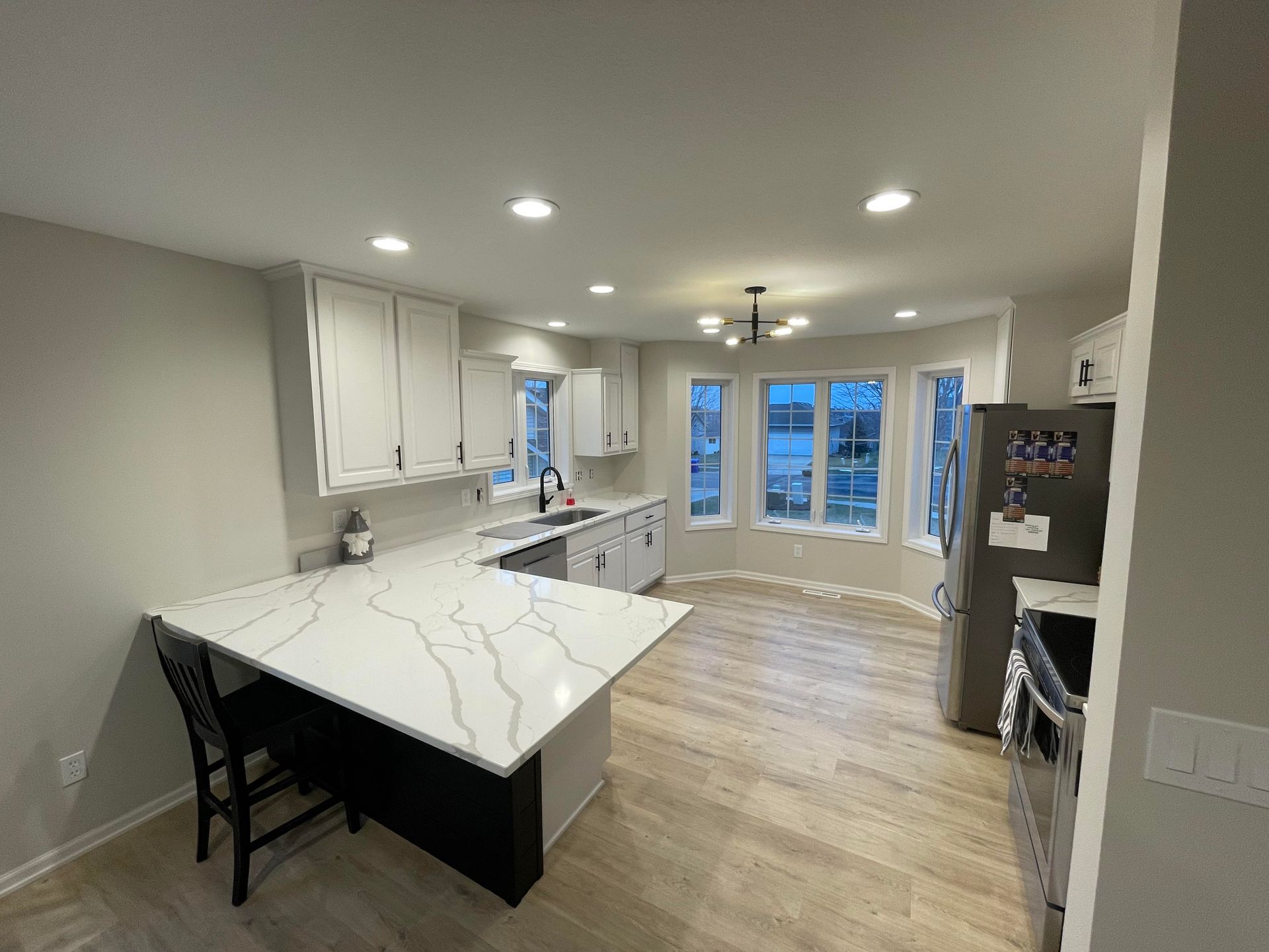 Modern kitchen with white cabinets, gray walls, and quartz countertops; dining area with large windows.
