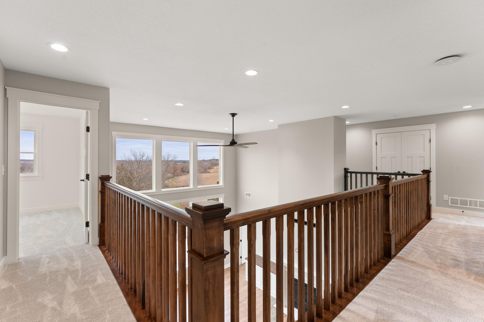 Interior view of a second-floor hallway with wood railing and carpeted floors, overlooking a lower level.