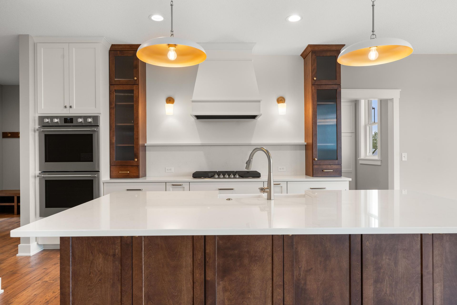 Modern kitchen with white countertops, dark wood island and cabinets, stainless steel appliances, and pendant lights.