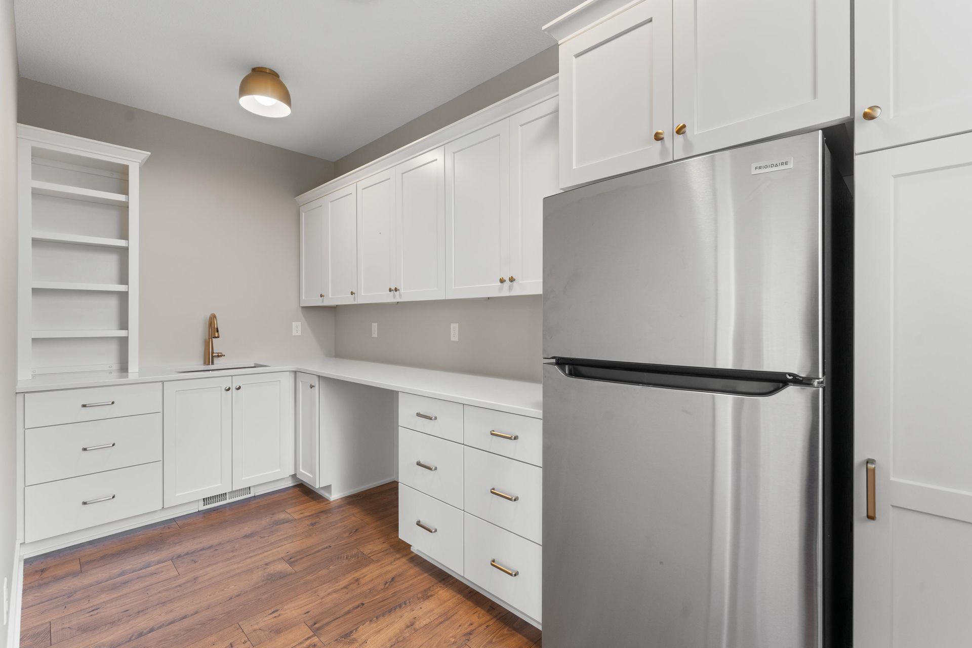 White cabinetry and stainless steel refrigerator in a well-lit kitchen with wood floors.