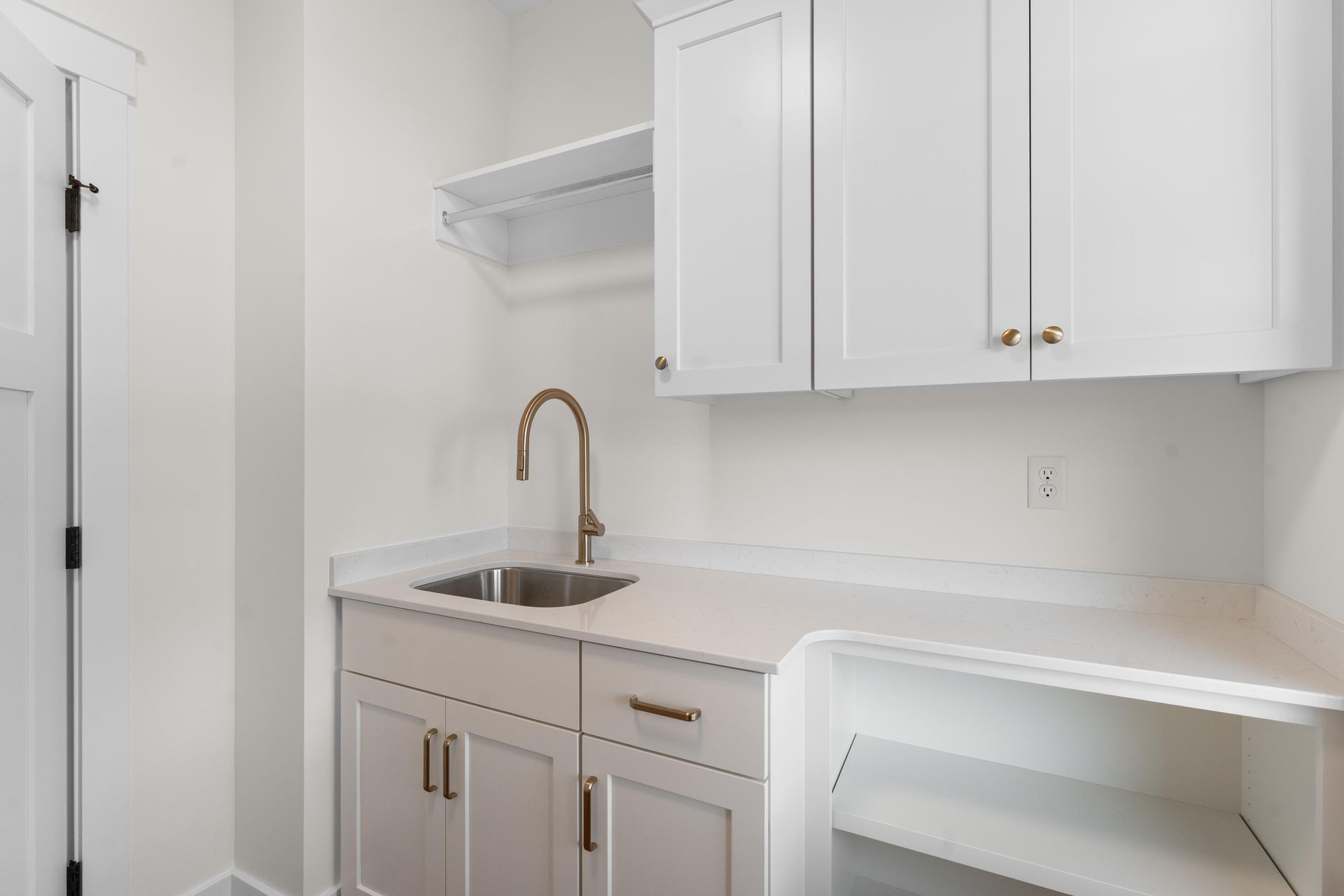 White laundry room with sink, cabinets, and open shelving.