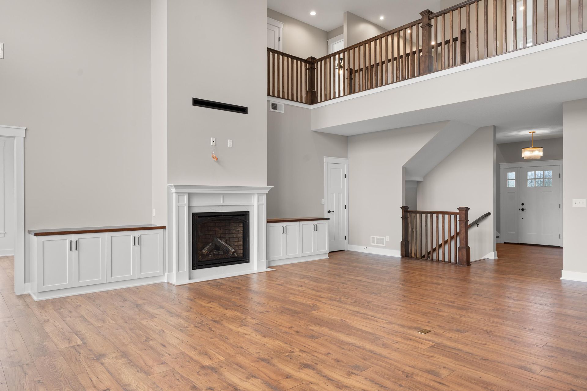 Spacious living room with fireplace, built-in cabinets, and hardwood floors. Staircase leads to a balcony.