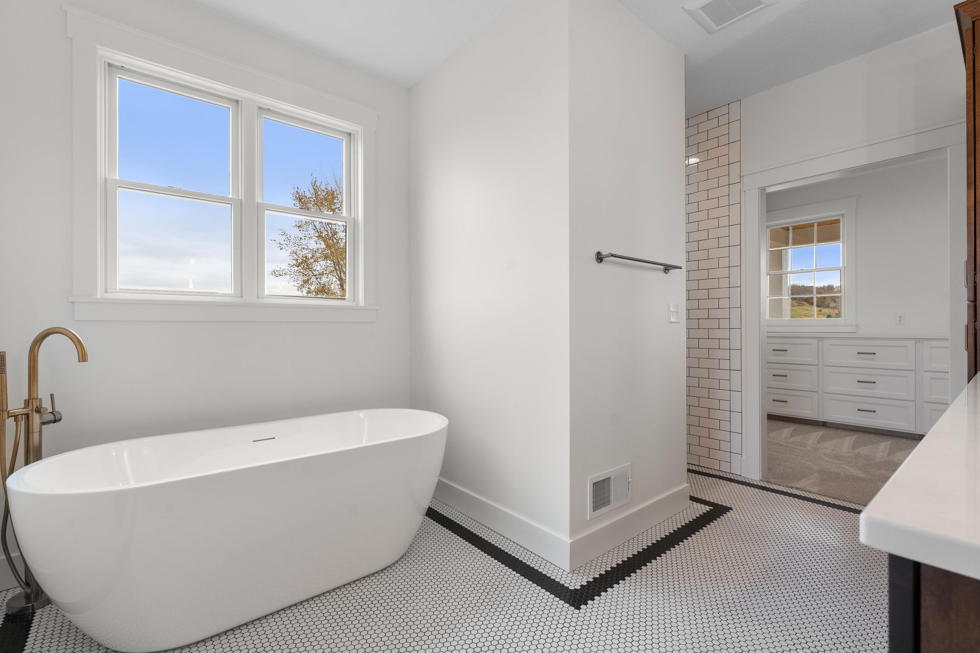 Modern white bathroom with a freestanding tub, window, and patterned tile floor.