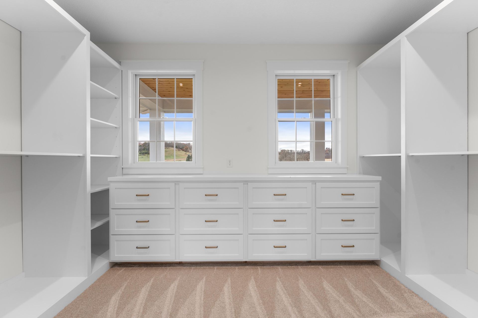 White closet with built-in drawers, shelves, and two windows looking outside, beige carpet.