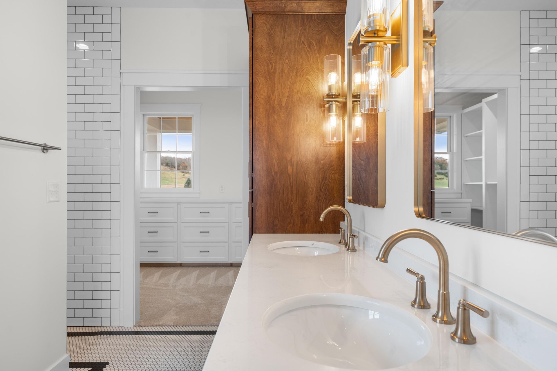Bathroom with double sinks, gold fixtures, white countertop, and walk-in closet in the background.