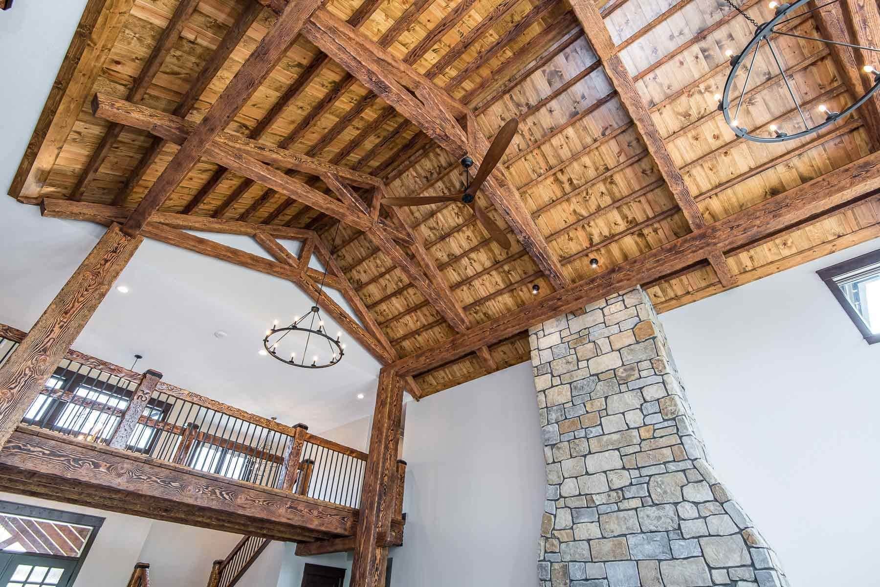 Wooden beams and ceiling in a rustic interior with stone fireplace and a loft.