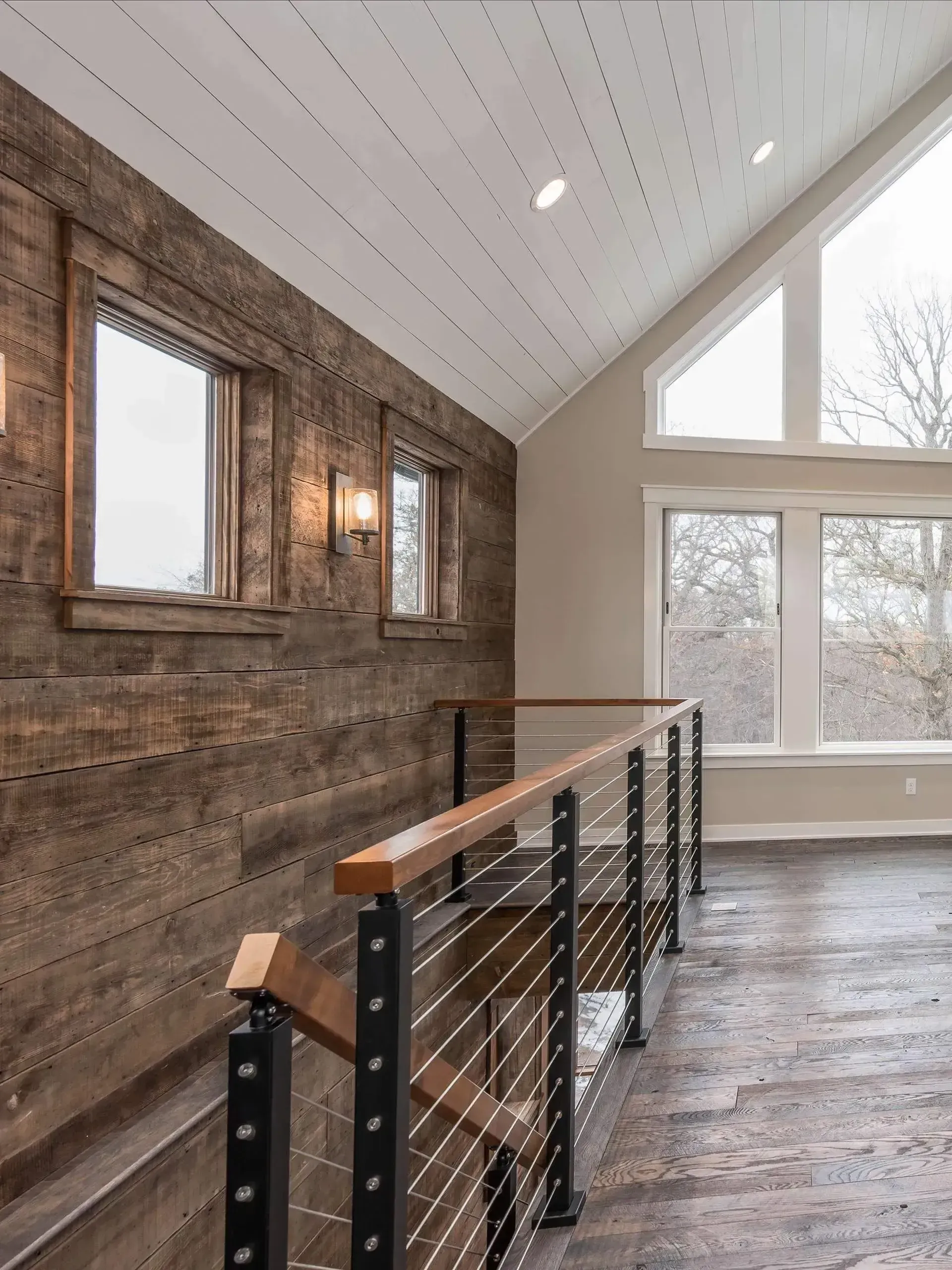 Interior view of a hallway with wood paneled walls, windows, and a cable railing.