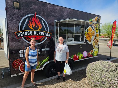 Food truck at night, lit with red lights, decorated with food images, and string lights on a nearby tent.