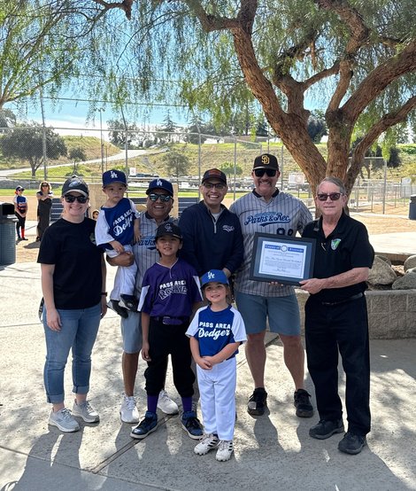 A group of adults and kids at Noble Creek ballpark holding a framed proclamation from a county supervisor recognizing the organization's first season.