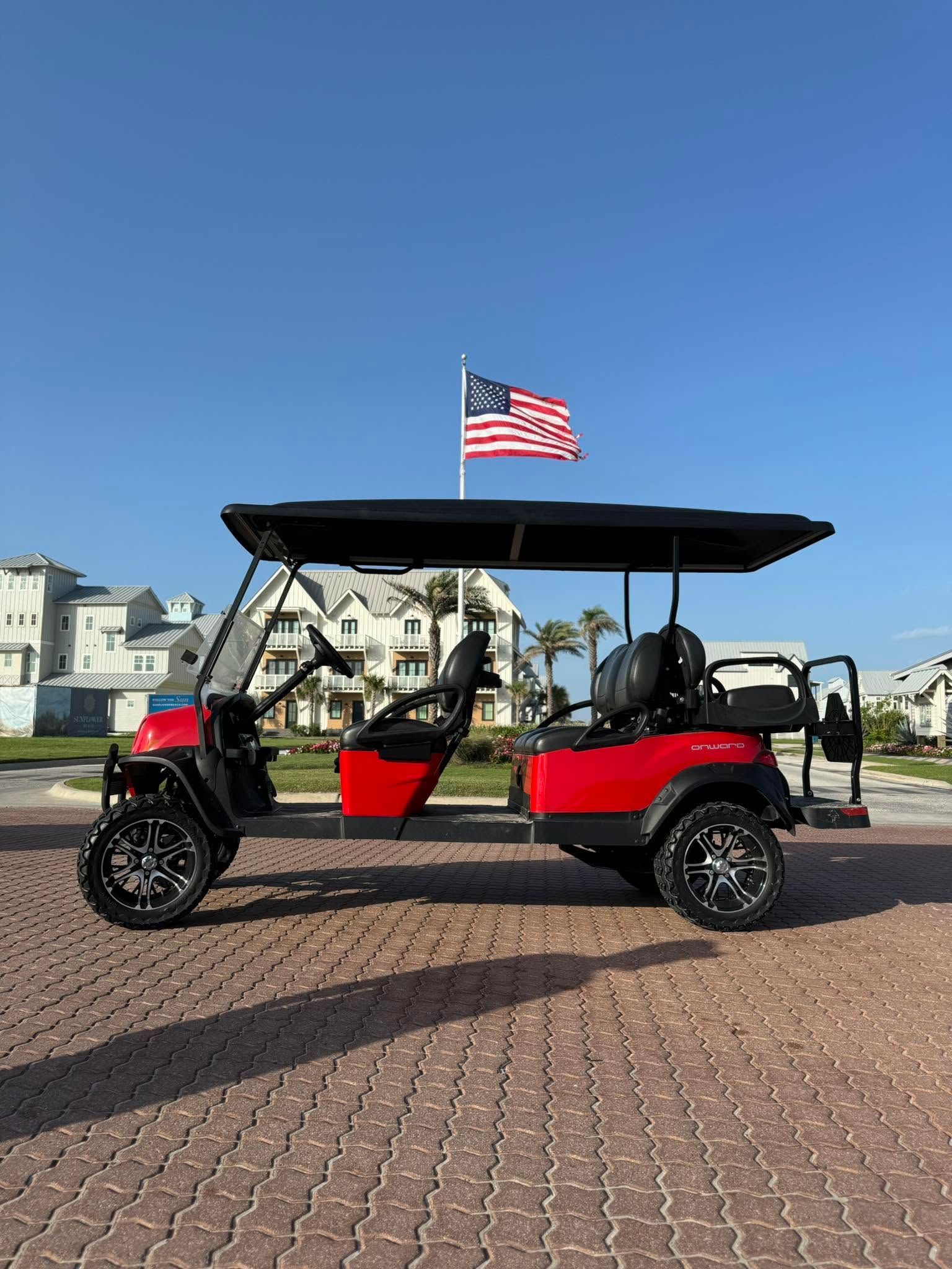 Red four-seat pedal cart with American flag parked on a brick promenade by the water