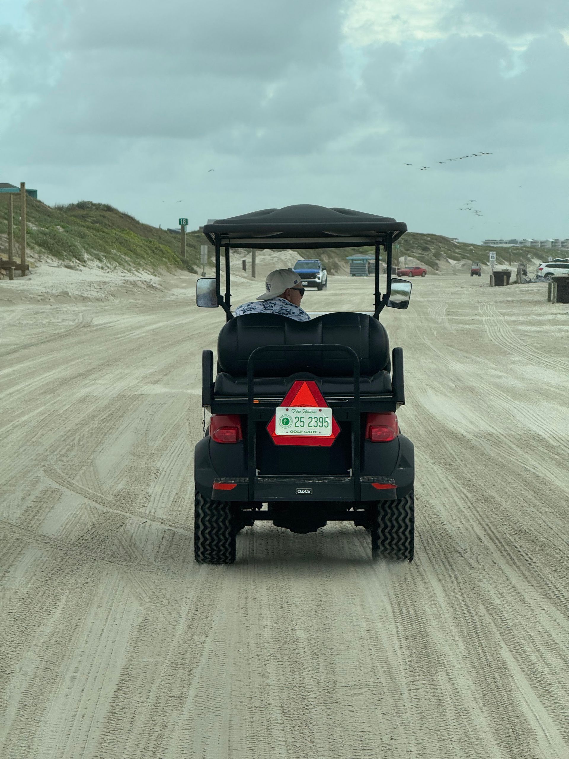 Golf cart driving on a sandy beach path, with dunes and ocean in the background.