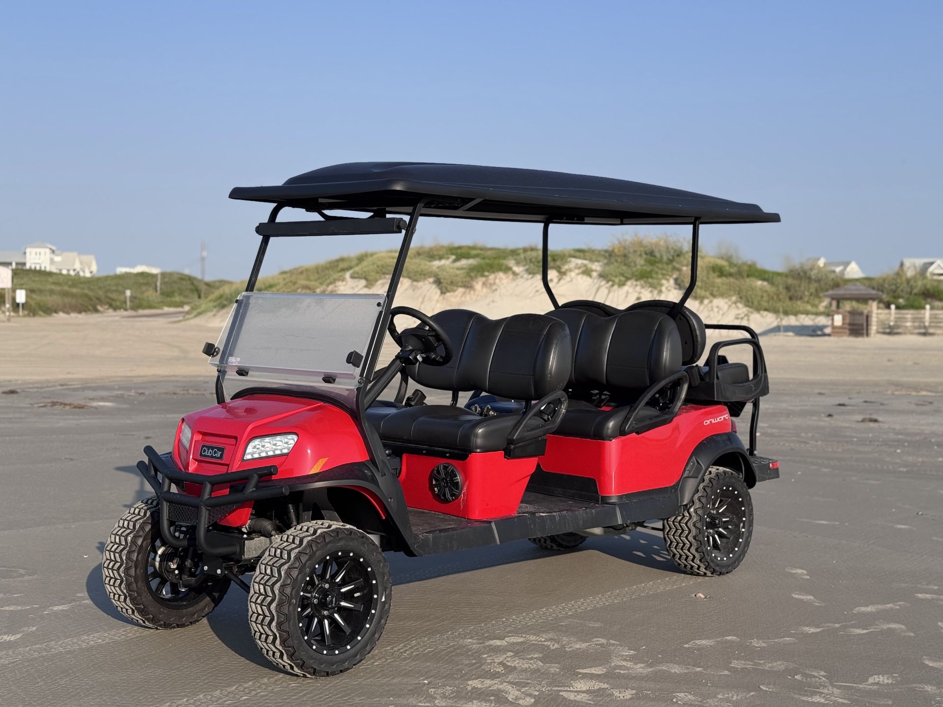 Red six-seat off-road utility cart with black roof parked on a sandy beach