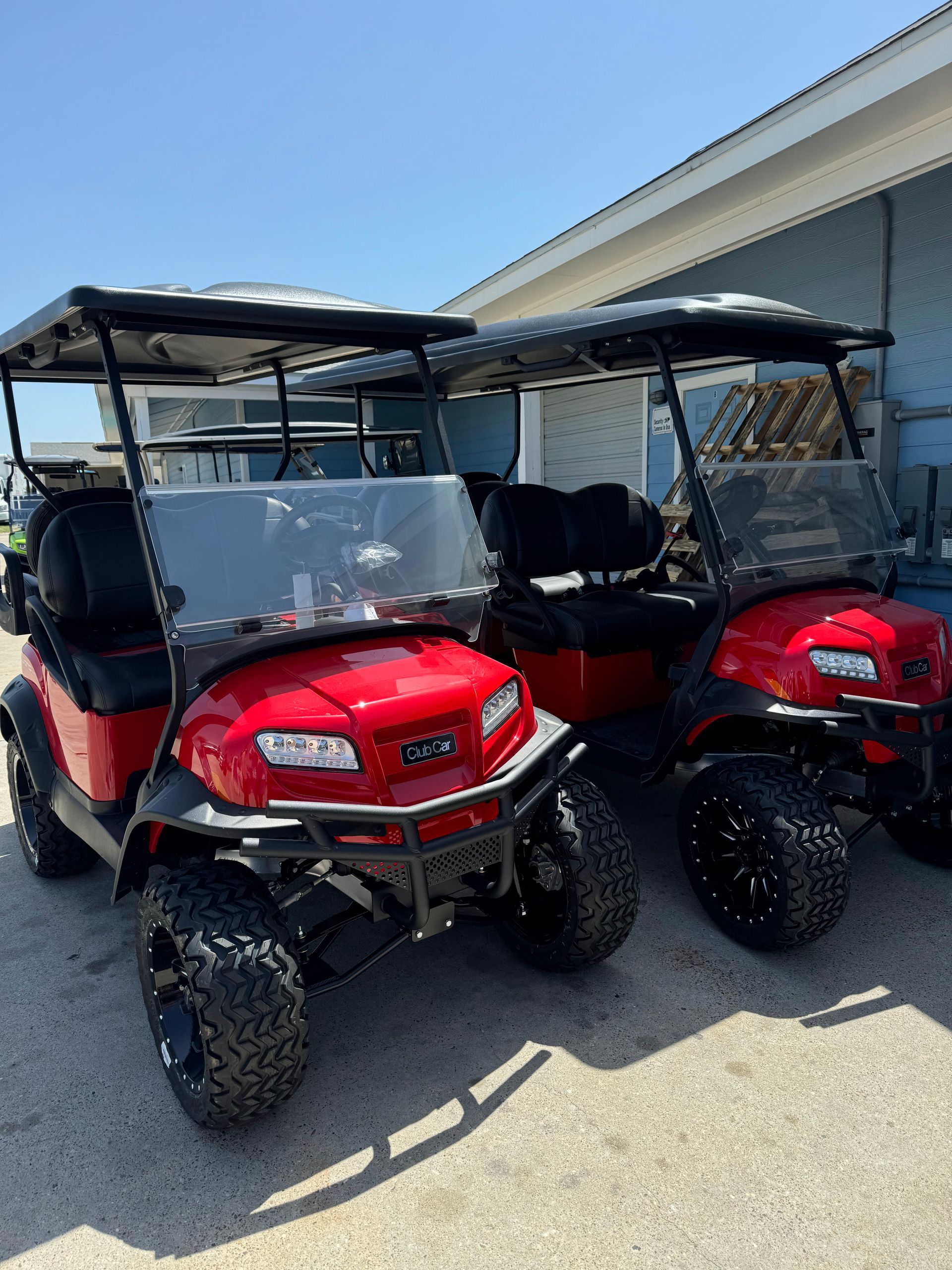 Two red side-by-side off-road utility carts parked outside a building
