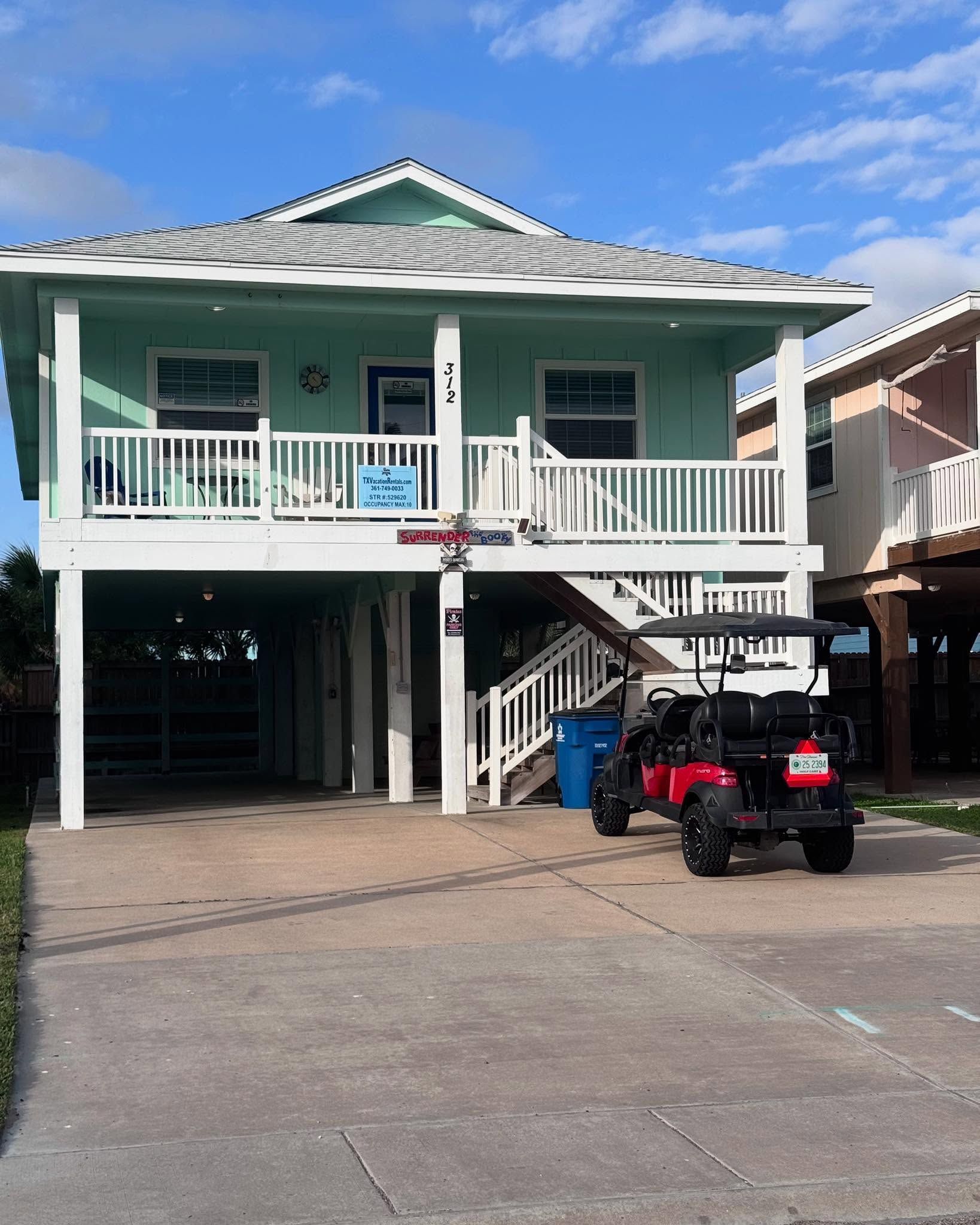 Mint-green raised house with white balcony and two parked ATVs in the driveway
