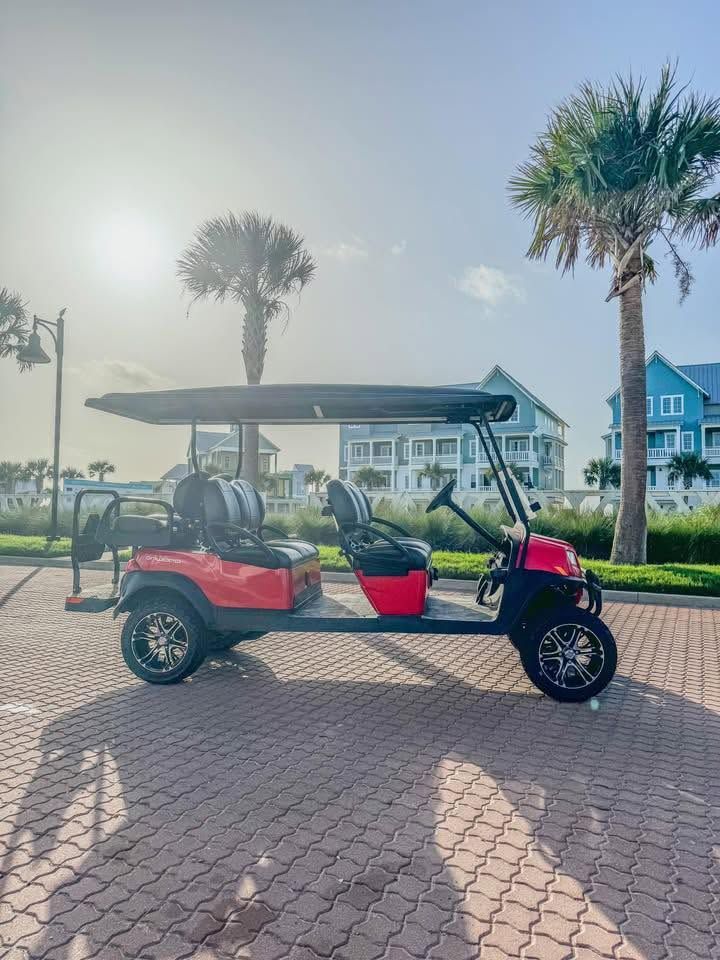 Red golf cart parked on a brick path near palm trees by the waterfront at sunrise