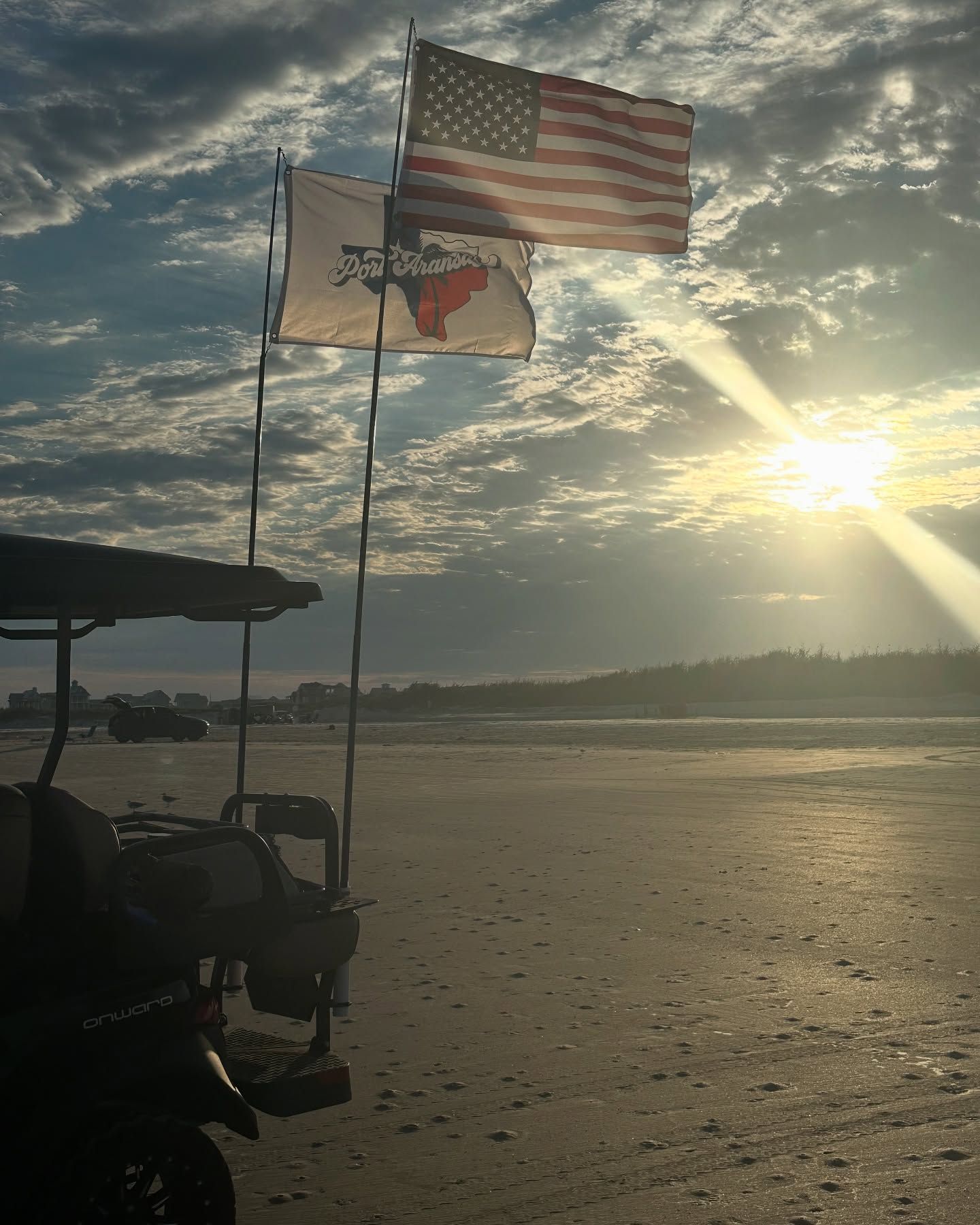 American and Texas flags flying by a calm beach at sunrise over the water