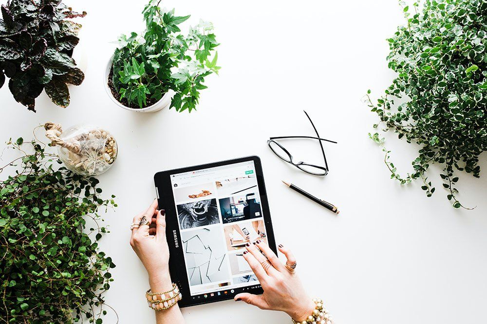 A woman is using a website on a tablet computer on a table surrounded by plants.