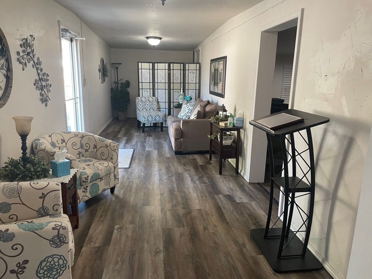 Bright living room with patterned chairs, wood floors, sofa, and console table near large windows