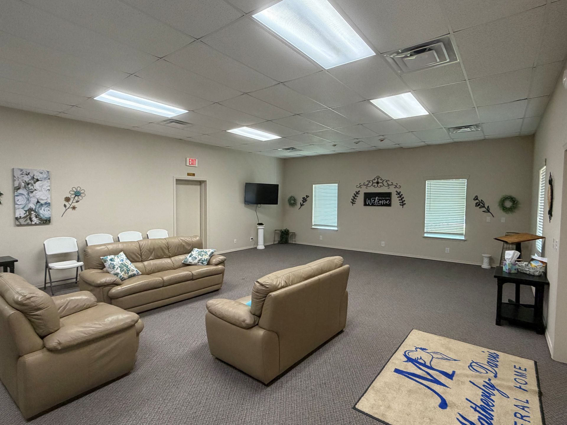 Spacious beige waiting room with sofas, chairs, wall art, and a small table under bright ceiling lights