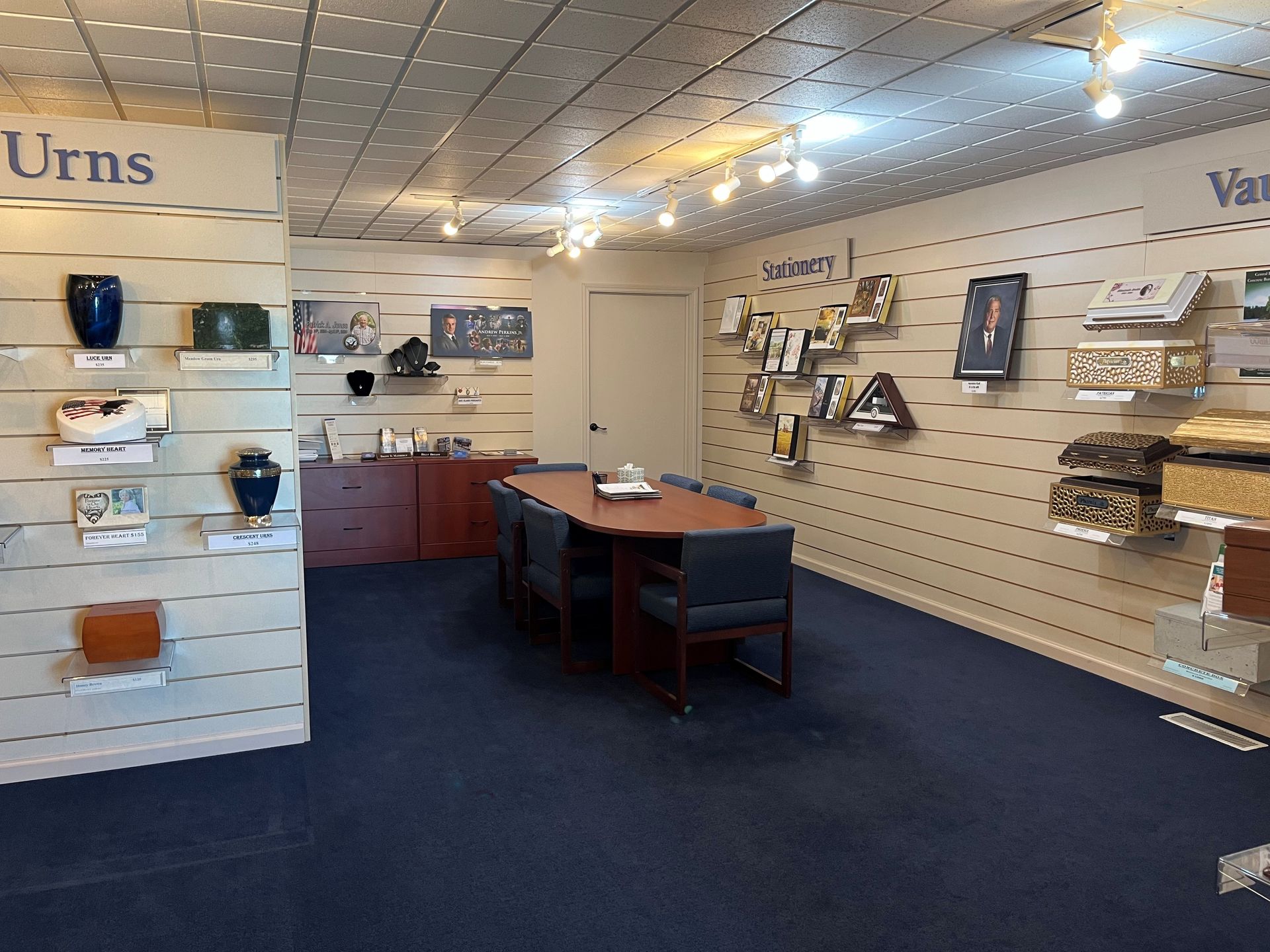 Display room with pegboard shelves, wooden desk, and assorted home products on white walls and blue carpet.