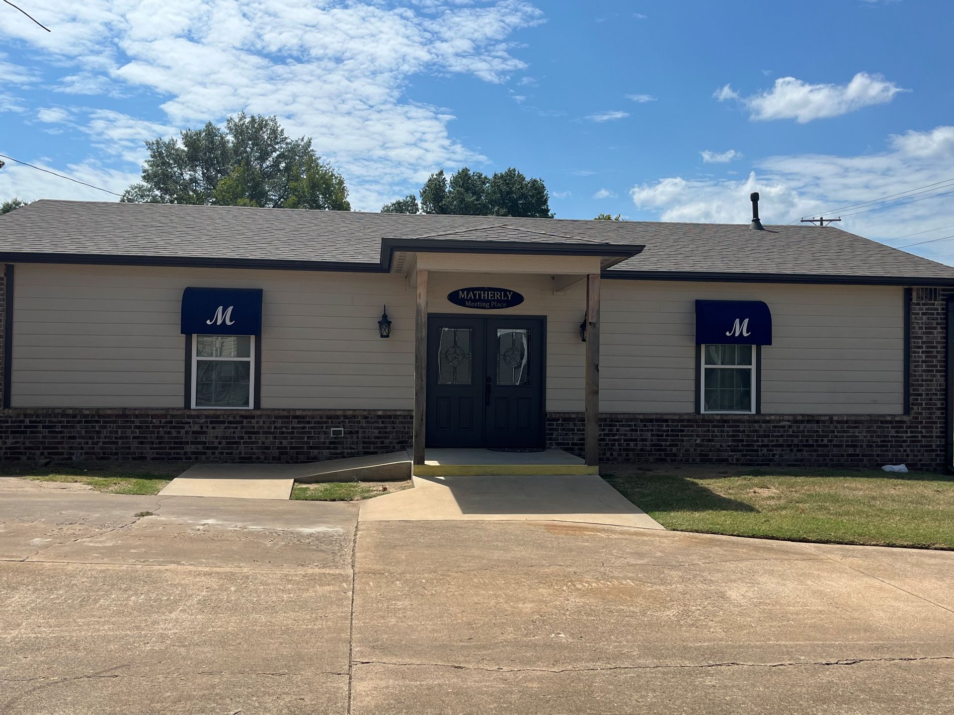 Single-story beige building with dark roof and blue window signs, centered entrance under a small porch.