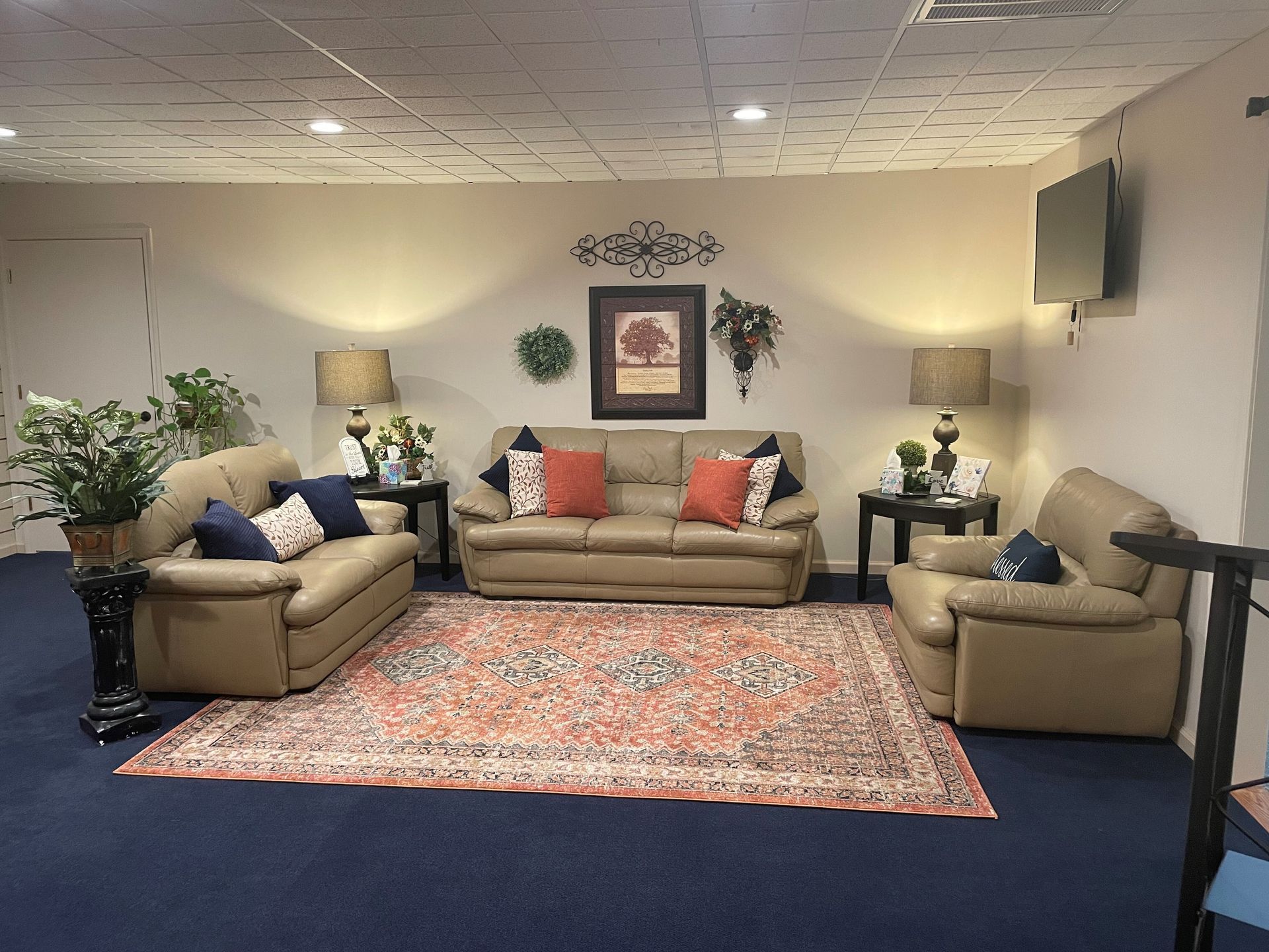 Living room with tan sofas, patterned rug, lamps, wall art, and plants
