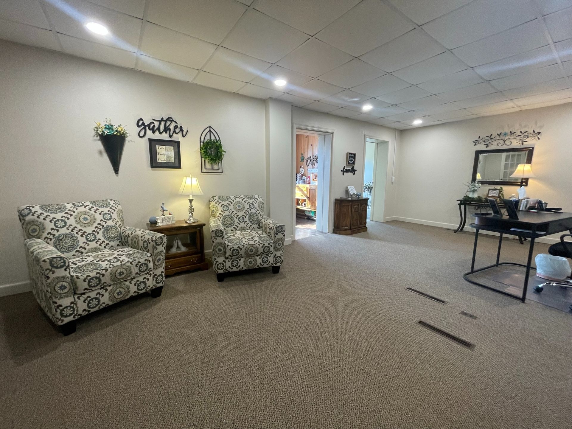 Spacious lobby with patterned chairs, side table, wall decor, and a desk in a carpeted waiting area