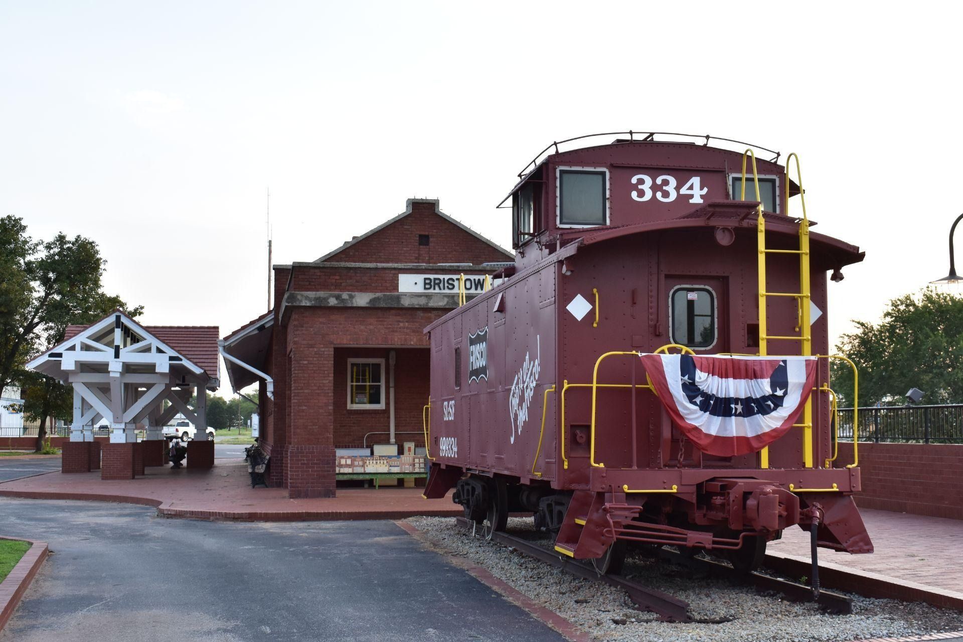Red caboose 334 at a train depot, decorated with red, white, and blue bunting.