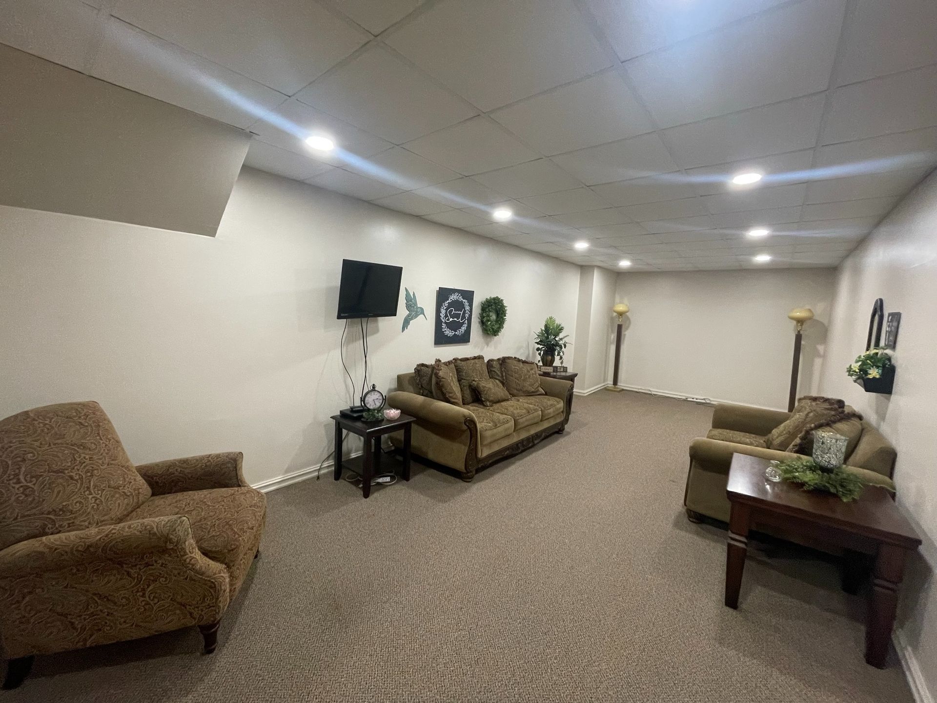 Spacious beige living room with couches, wall art, a TV, and a coffee table on carpeted floor.